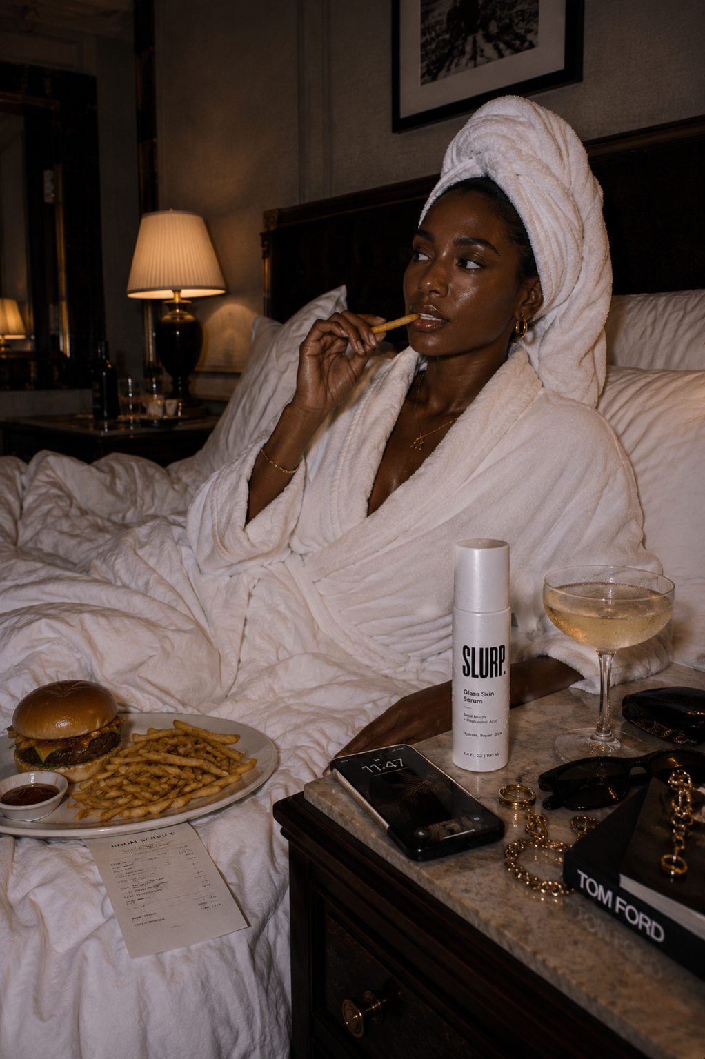 Woman in a hotel bathrobe with SLURP Glass Skin Serum, room service, and champagne
